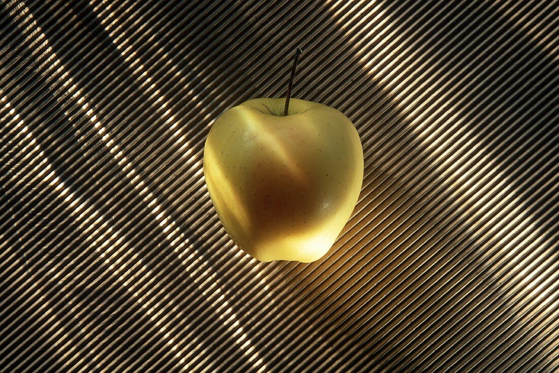 Ein Golden Delicious Apfel auf gestreiftem Untergrund