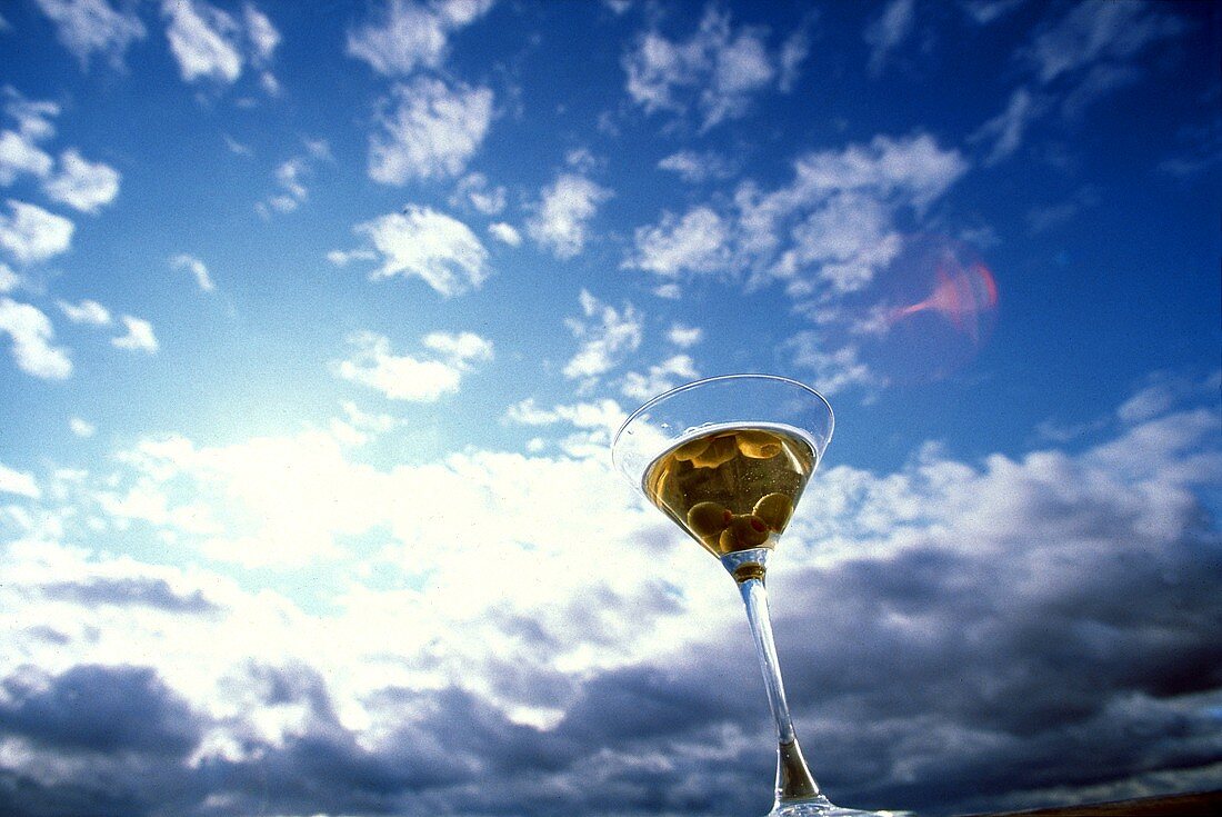 Martini mit Oliven in einem Glas vor blauem Himmel mit Wolken