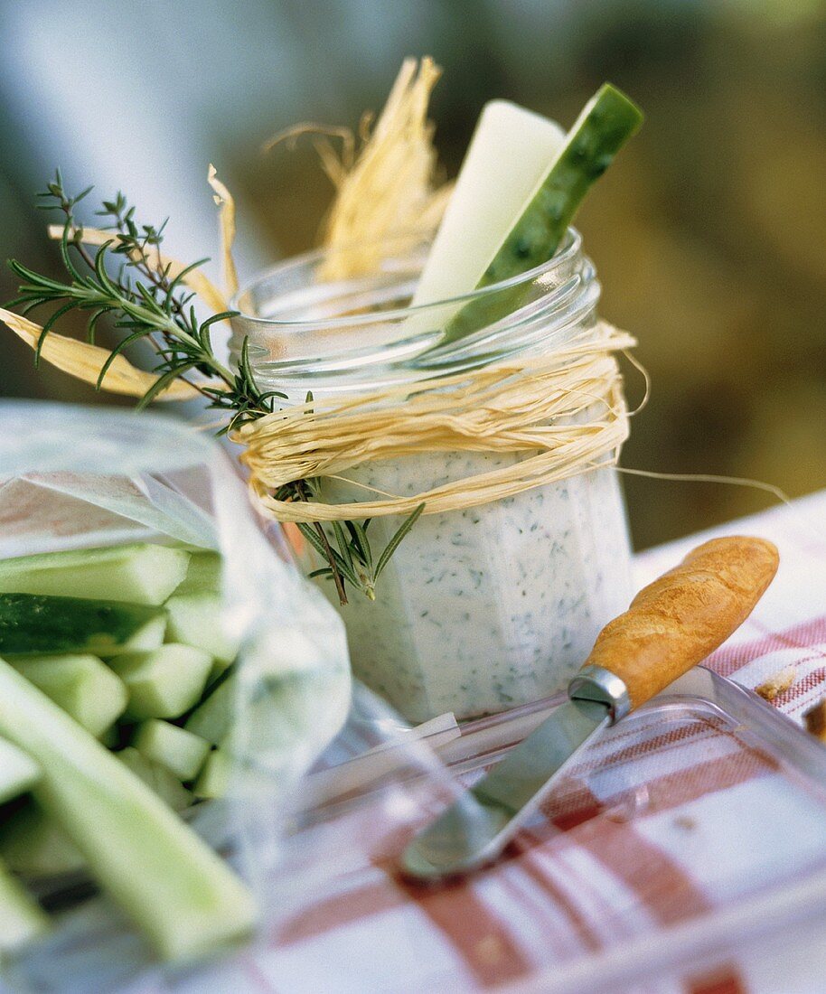 Kräuterdip in Glas mit Gurkenstäbchen zum Picknick