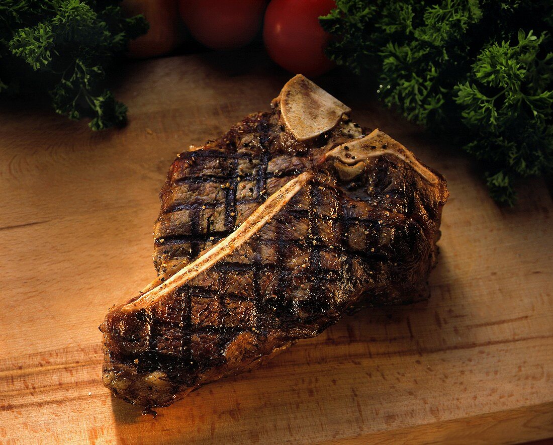 Gegrilltes T-Bone Steak auf Schneidebrett; Tomaten, Kräuter