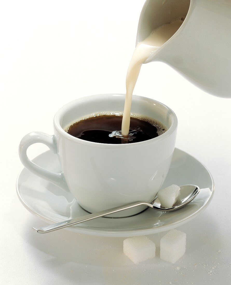 Sahne wird in eine Tasse mit schwarzem Kaffee gegossen