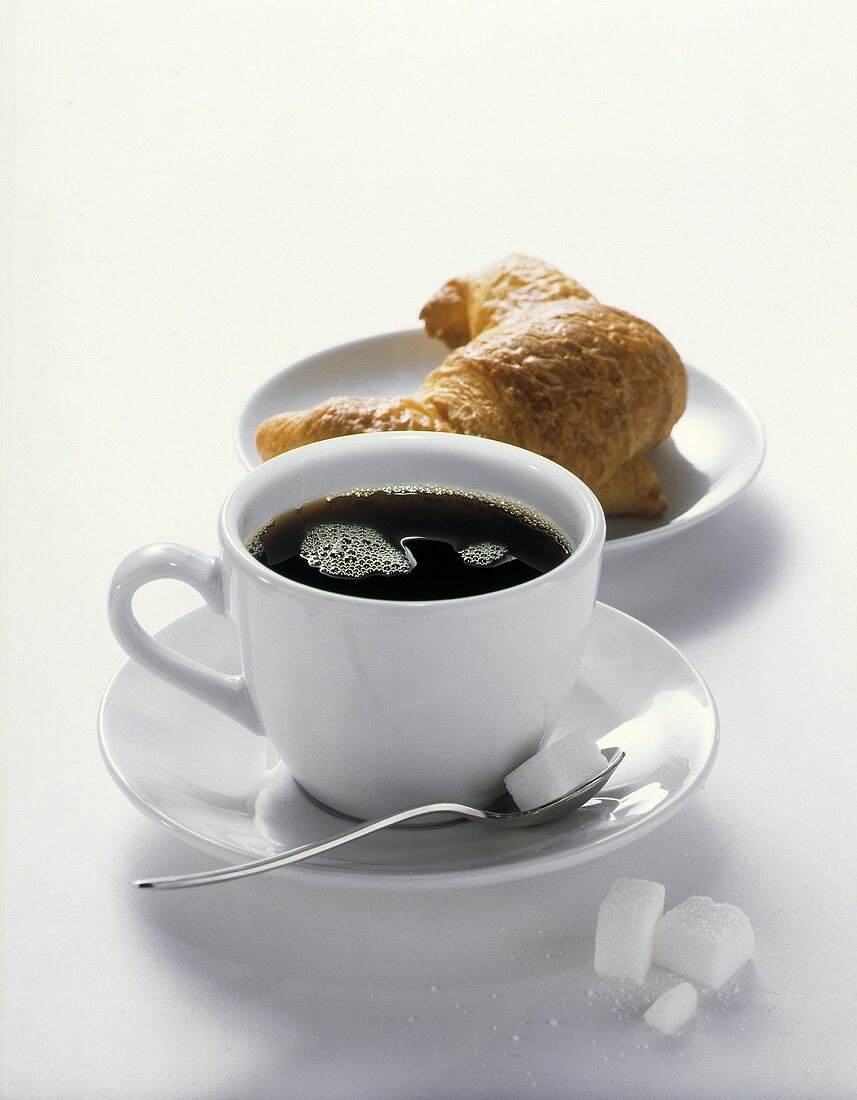 Schwarzer Kaffee in weisser Tasse, Zuckerwürfel & Croissant