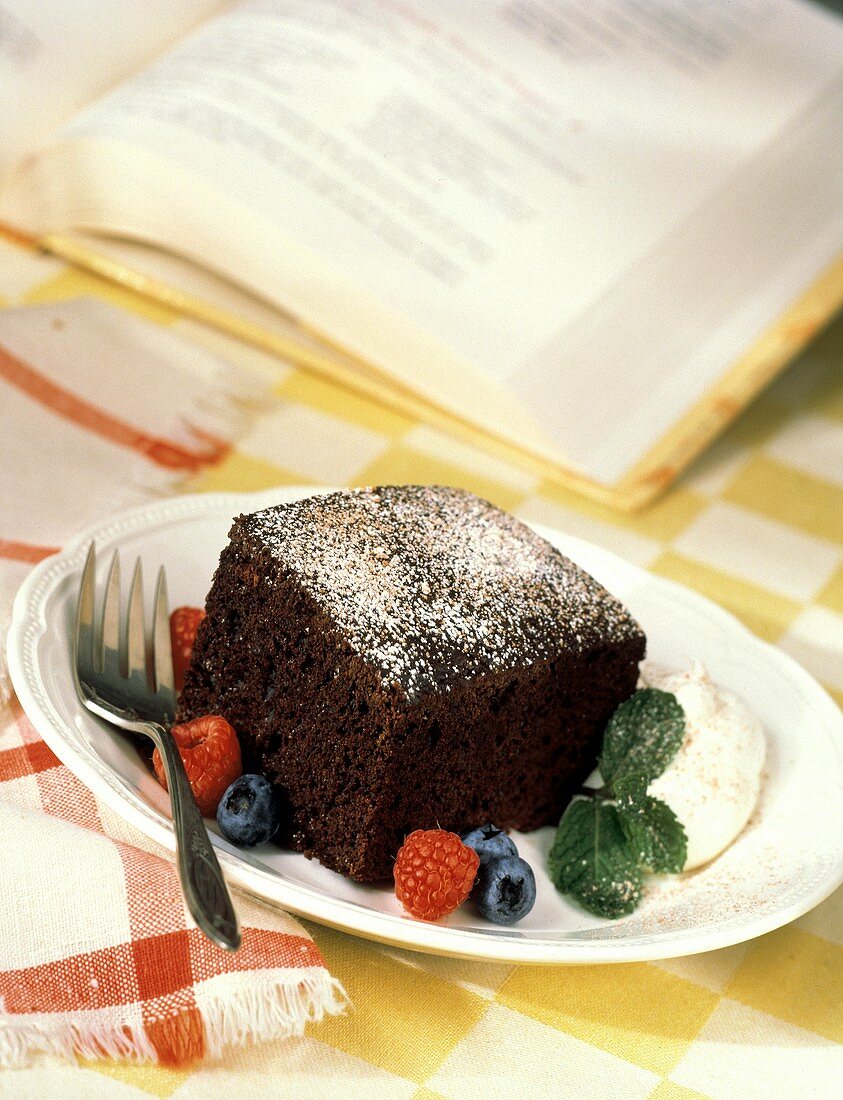 Ein Stück Schokoladenkuchen mit Puderzucker, Sahne & Beeren