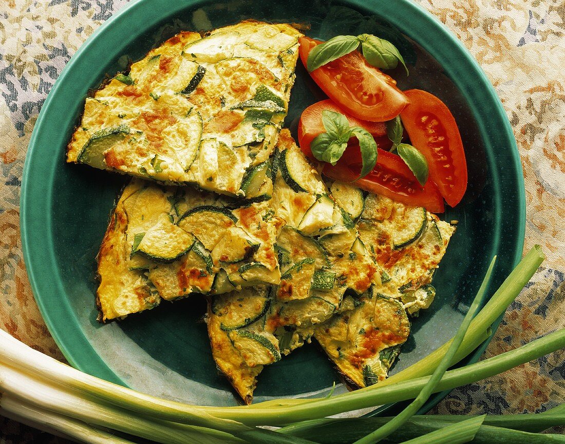 Frittata mit Zucchini auf grünem Teller, garniert mit Tomaten