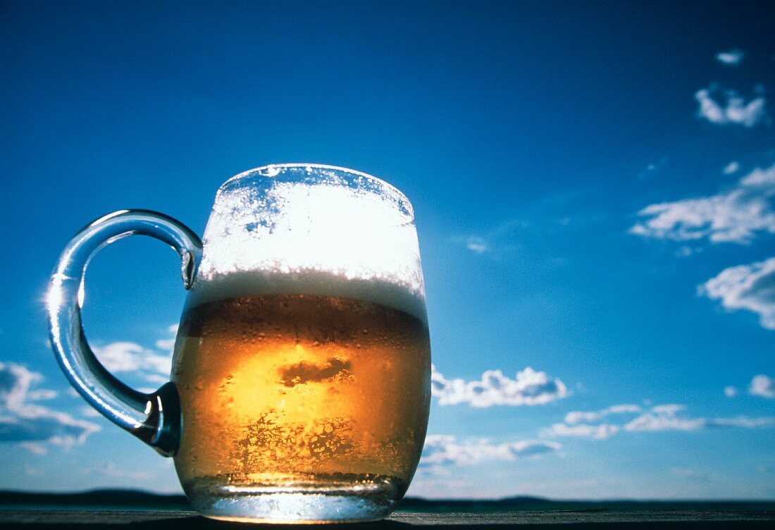 Helles Bier im Glaskrug im Gegenlicht vor blauem Himmel