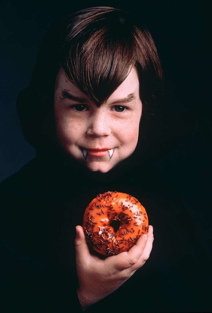 Kleiner Junge als Dracula verkleidet hält Donut in der Hand