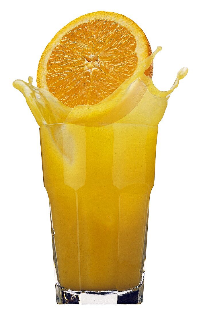Orangenhälfte fällt in ein Glas mit Orangensaft