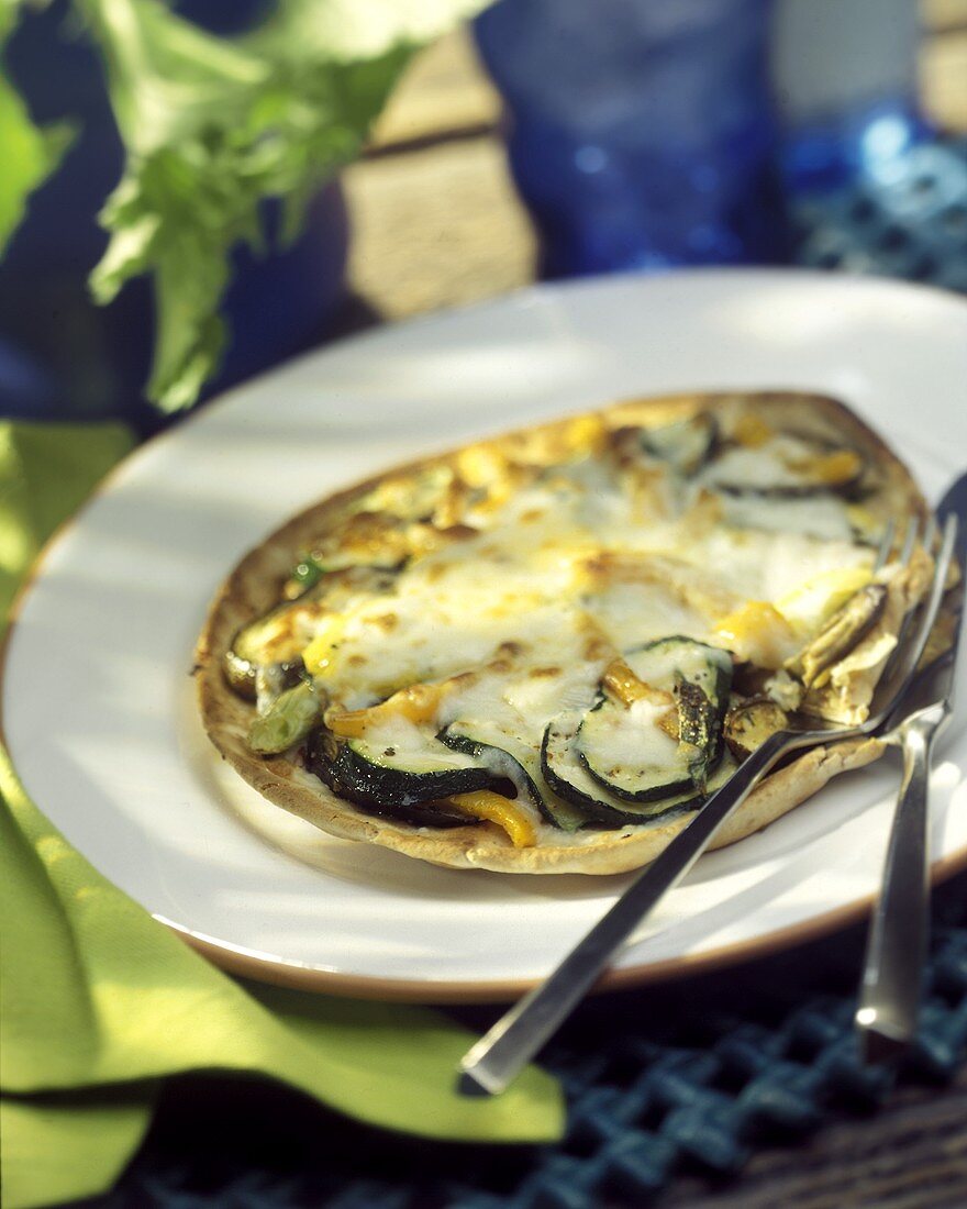 Pitabrotpizza mit Zucchini auf weißem Teller mit Besteck