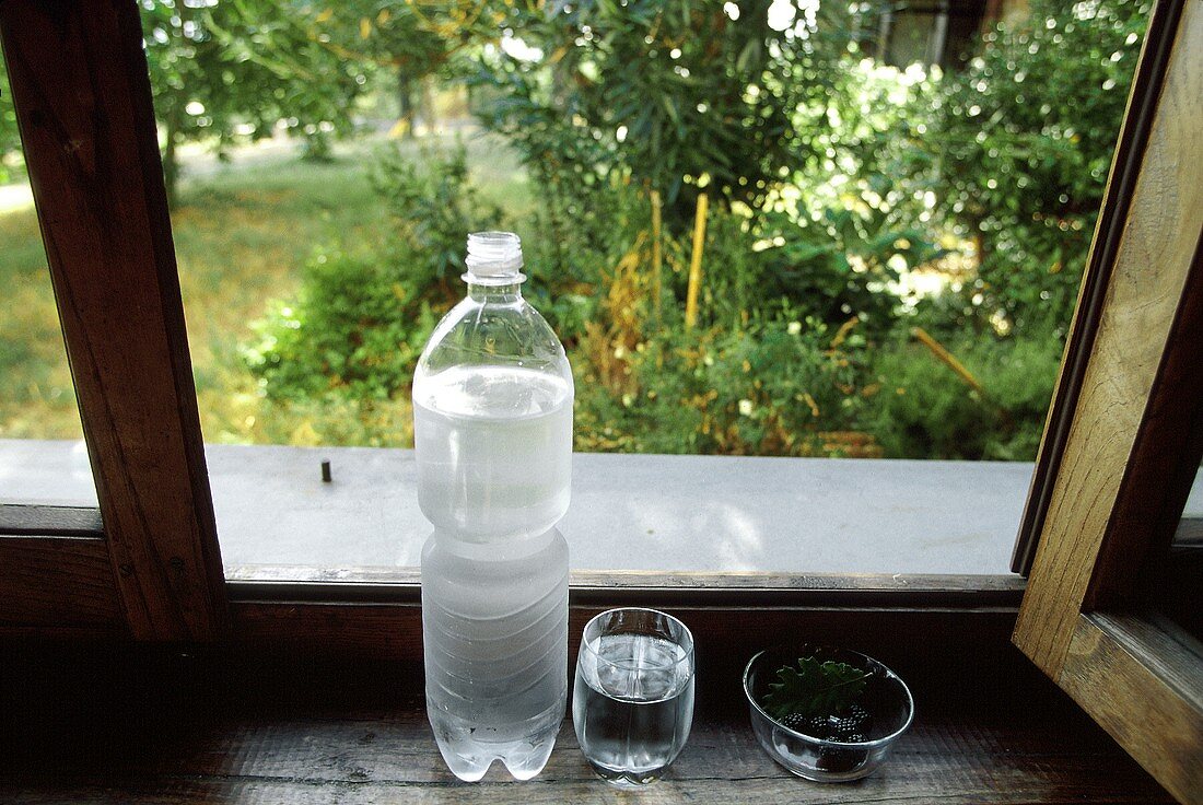 Flasche und Glas Mineralwasser an einem offenen Fenster
