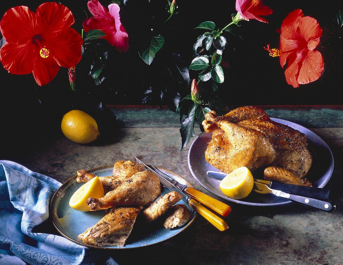 Brathähnchen mit Zitronen auf zwei Tellern; Deko: Blumen