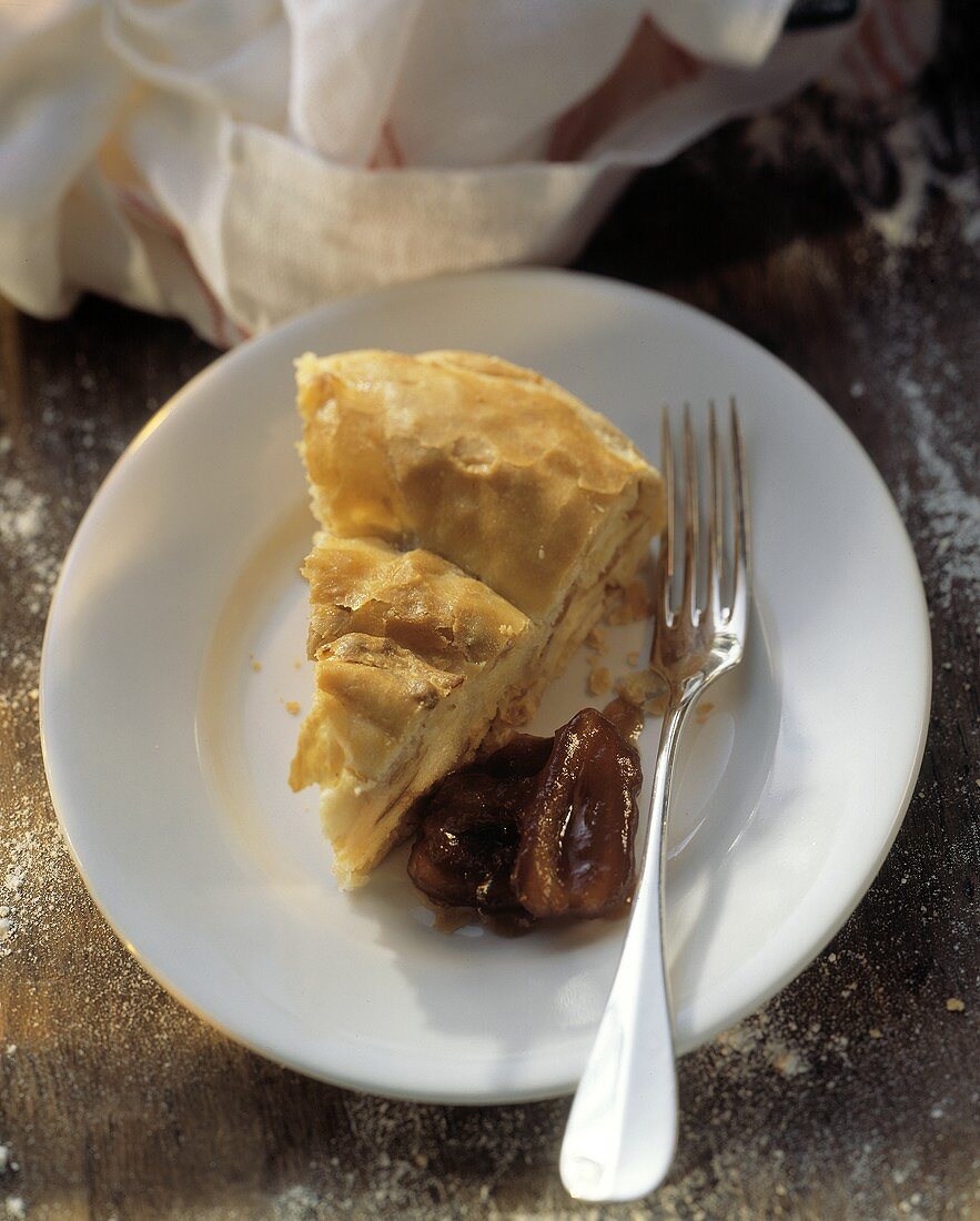 Ein Stück Apfel-Kugel, daneben Pflaumen und Gabel auf Teller