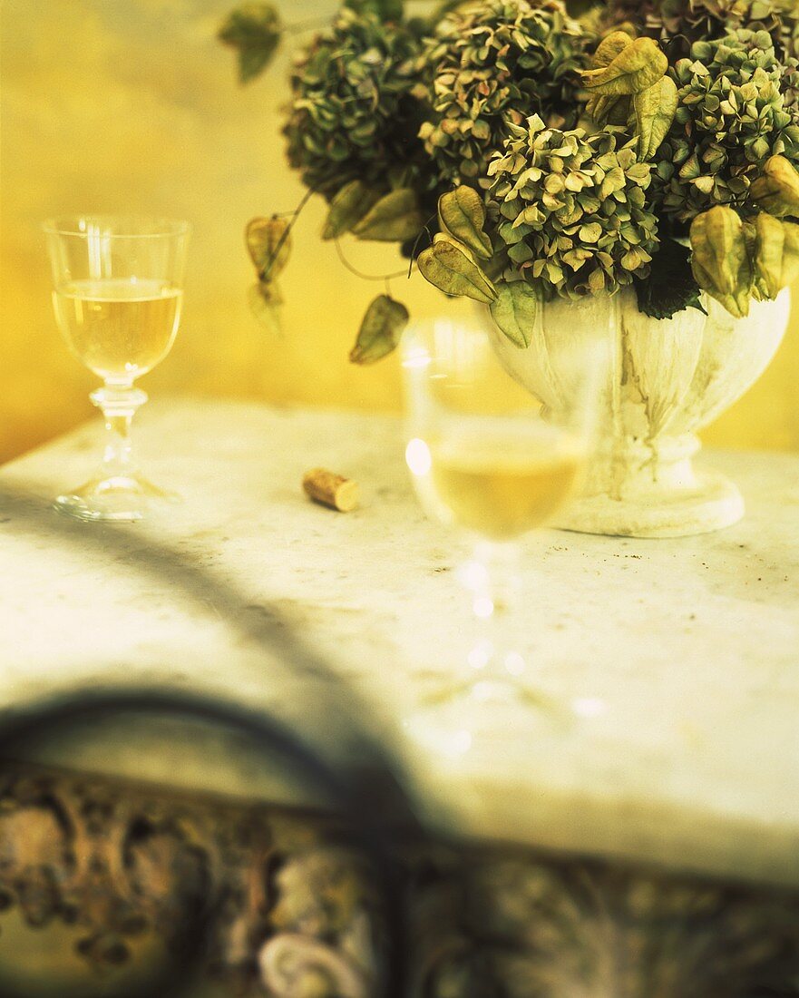 Zwei Gläser Weißwein und Blumenvase mit getrockneten Blumen
