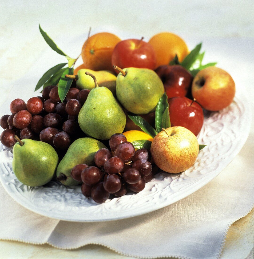 Birnen, Äpfel, Trauben und Orangen auf weisser Platte