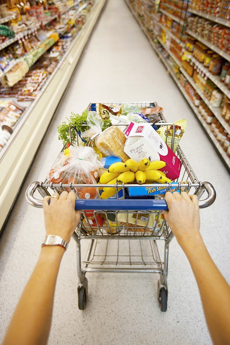 Hände schieben vollen Einkaufswagen durch einen Supermarkt
