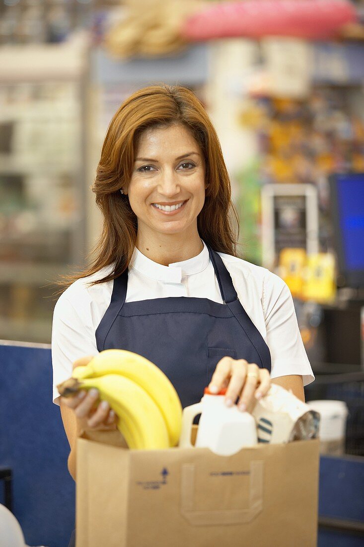 Kassiererin im Supermarkt füllt Bananen in braune Papiertüte