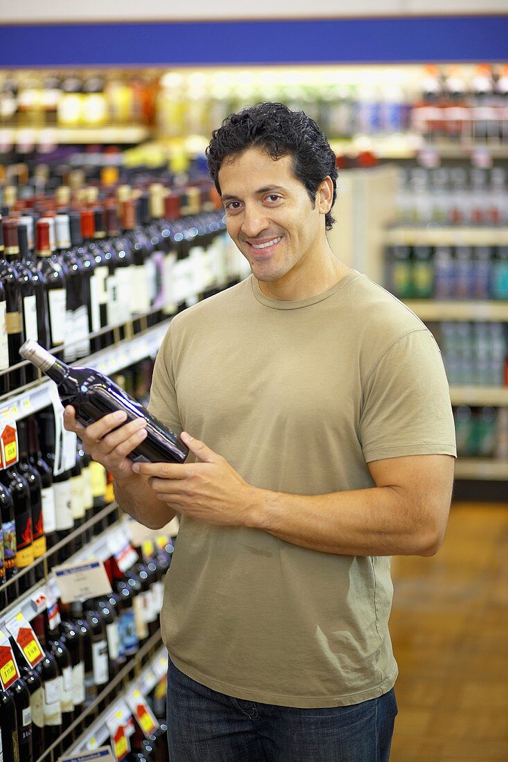 Lächelnder Mann hält Weinflasche im Supermarkt