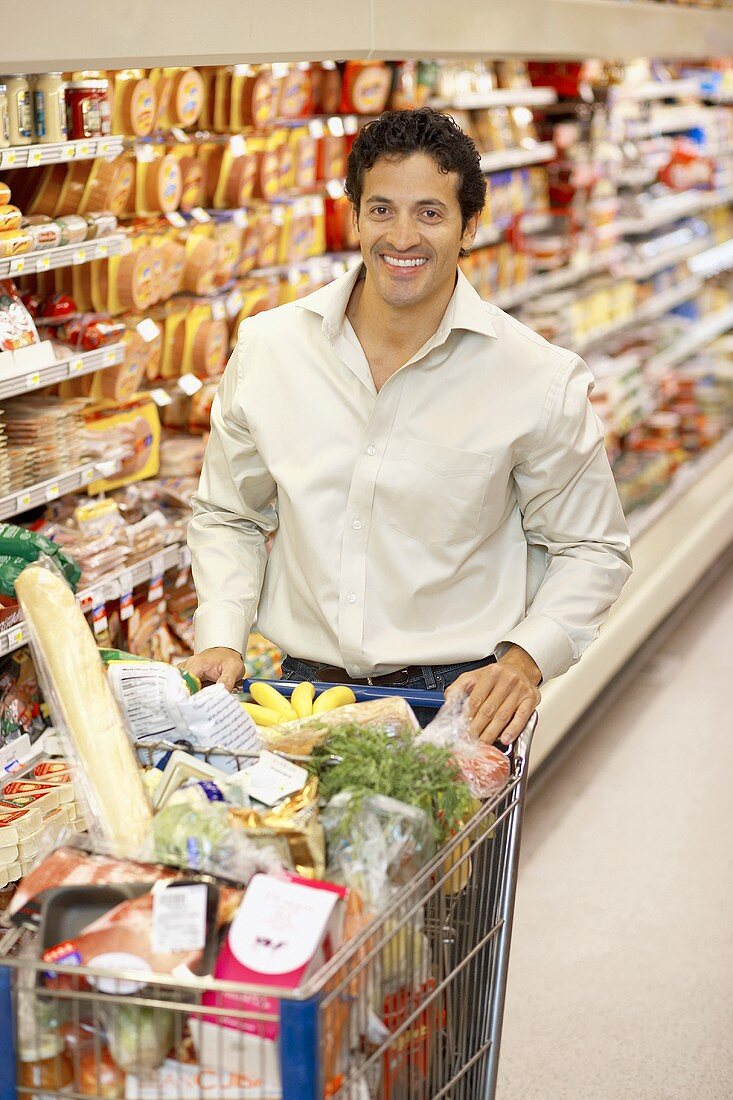 Lächelnder Mann schiebt vollen Einkaufswagen im Supermarkt