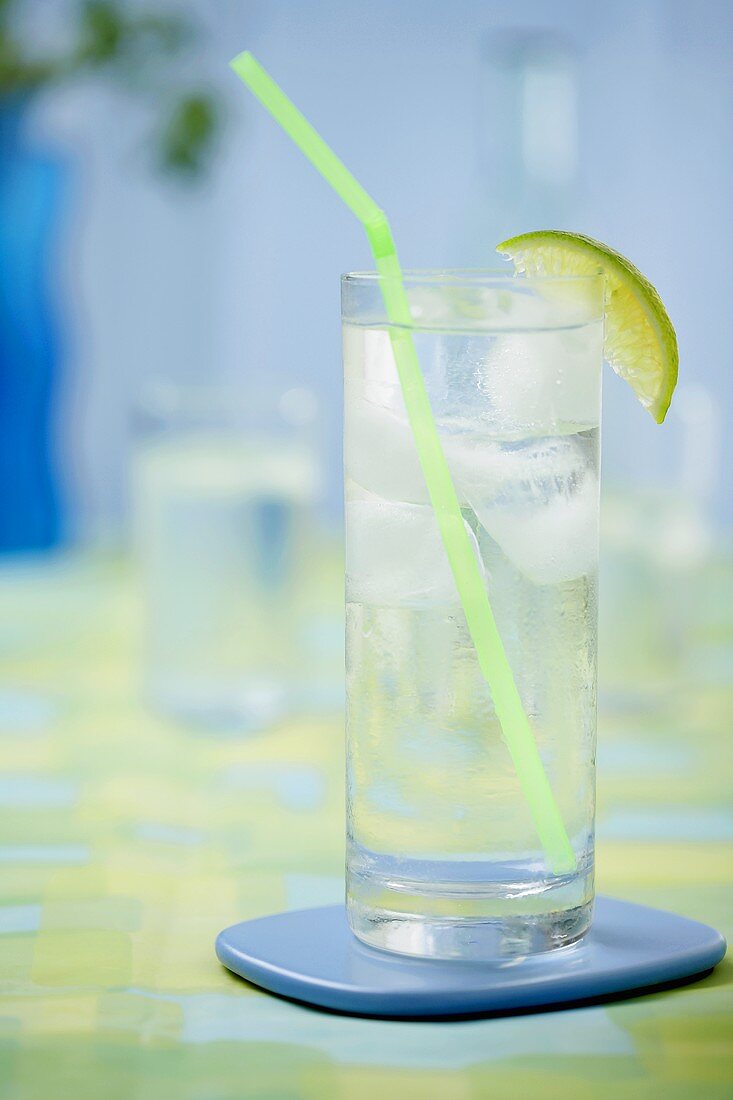 Glass of water with lime wedge, ice cubes and straw