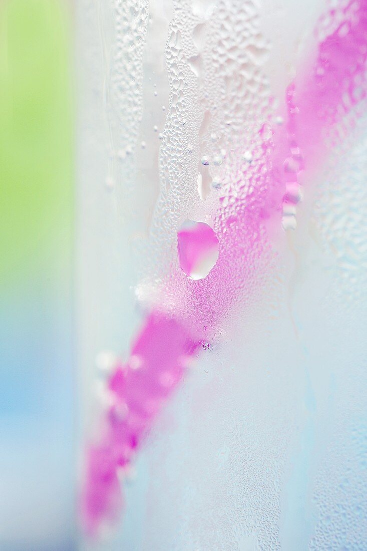 Glas Eiswasser mit Wassertropfen und rosa Strohhalm
