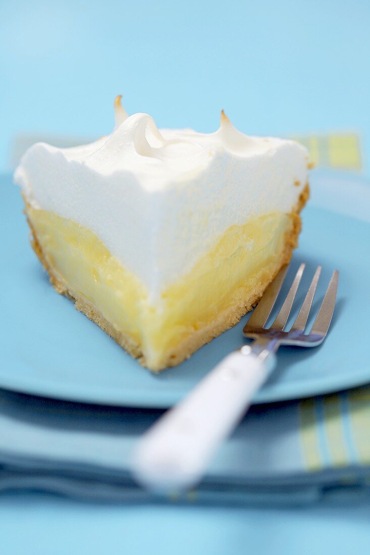 Piece of lemon meringue pie on blue plate with fork (USA)