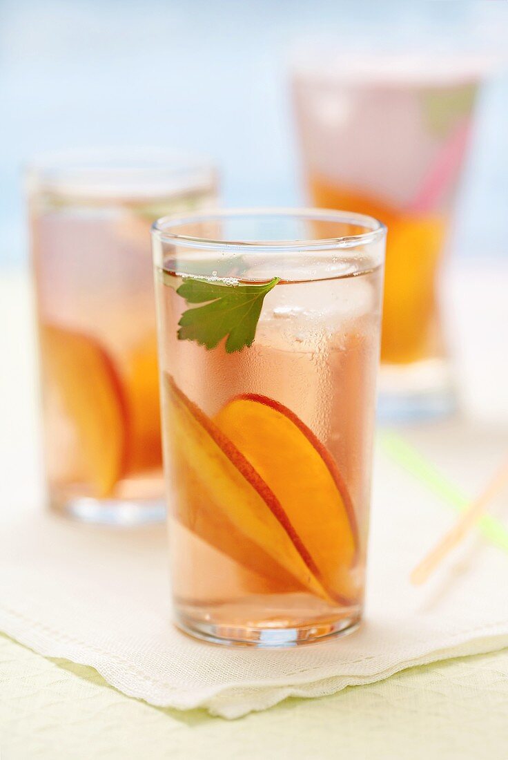Three glasses of iced tea with peach slices on napkin