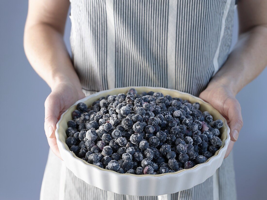 Person holding unbaked blueberry pie