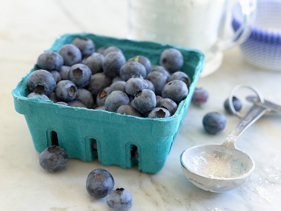 Fresh blueberries in cardboard punnet, measuring spoon