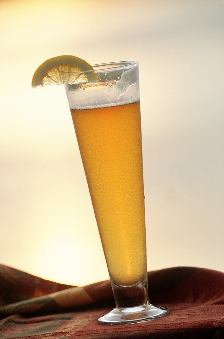 Large glass of light wheat beer with lemon wedge outdoors