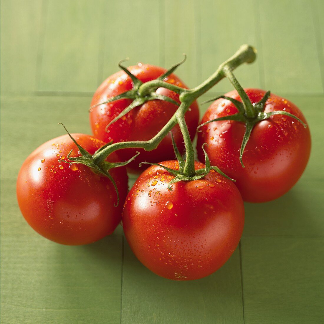 Four vine tomatoes with drops of water on green background