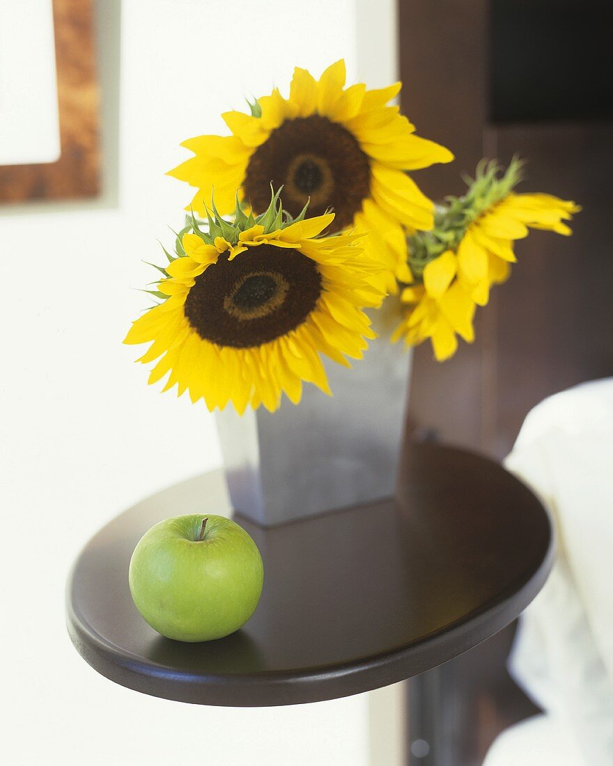 Stillleben mit Sonnenblumen und einem grünen Apfel