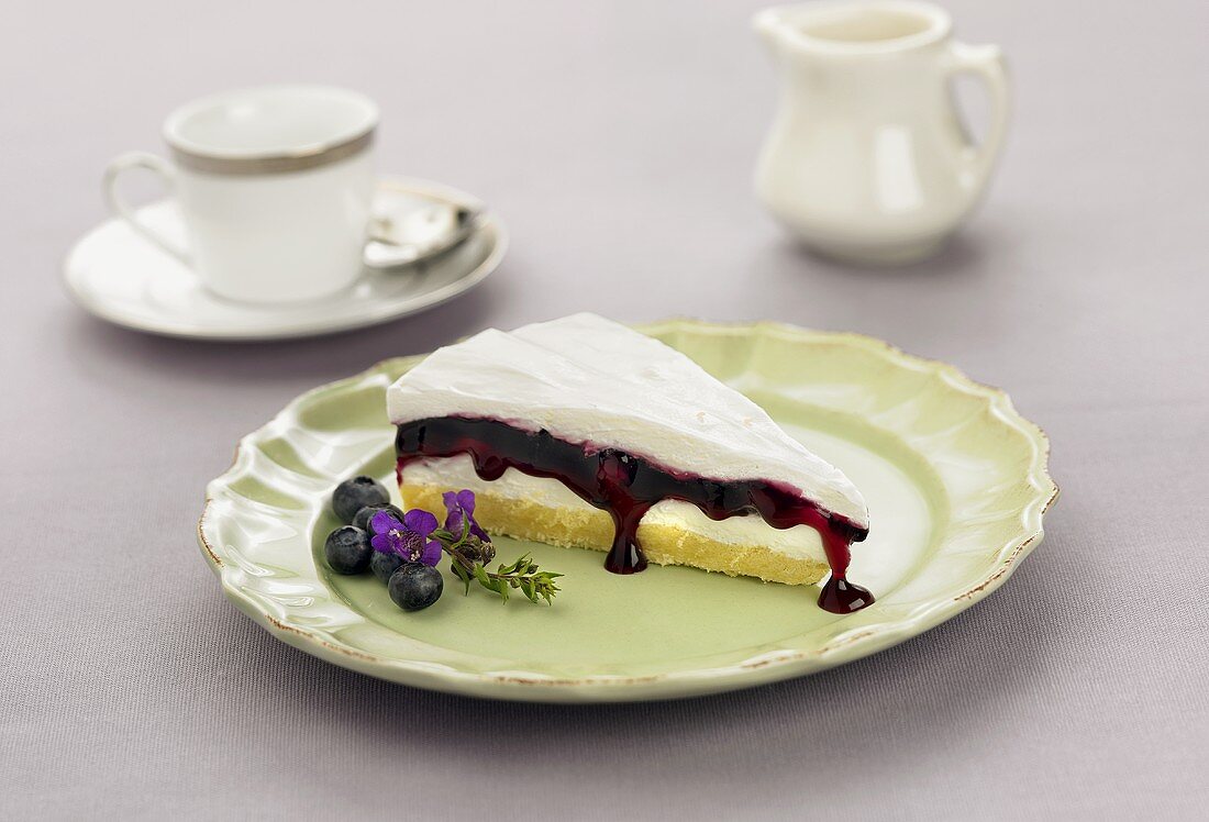 Slice of Layered Cake with Blueberry Filling on a Plate, Tea Cup and Pitcher