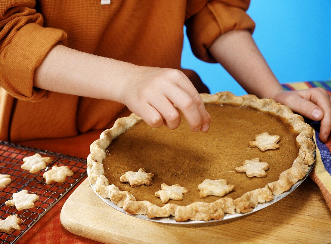 Child Placing Leaf Shaped Pie Crust Cut Outs on the Top of a Pumpkin Pie