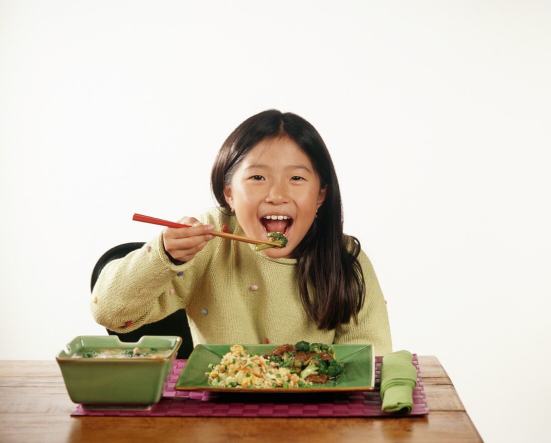 Child Eating a Piece of Broccoli with Chopsticks, Plate of Broccoli Stir Fry and Fried Rice, Bowl of Soup