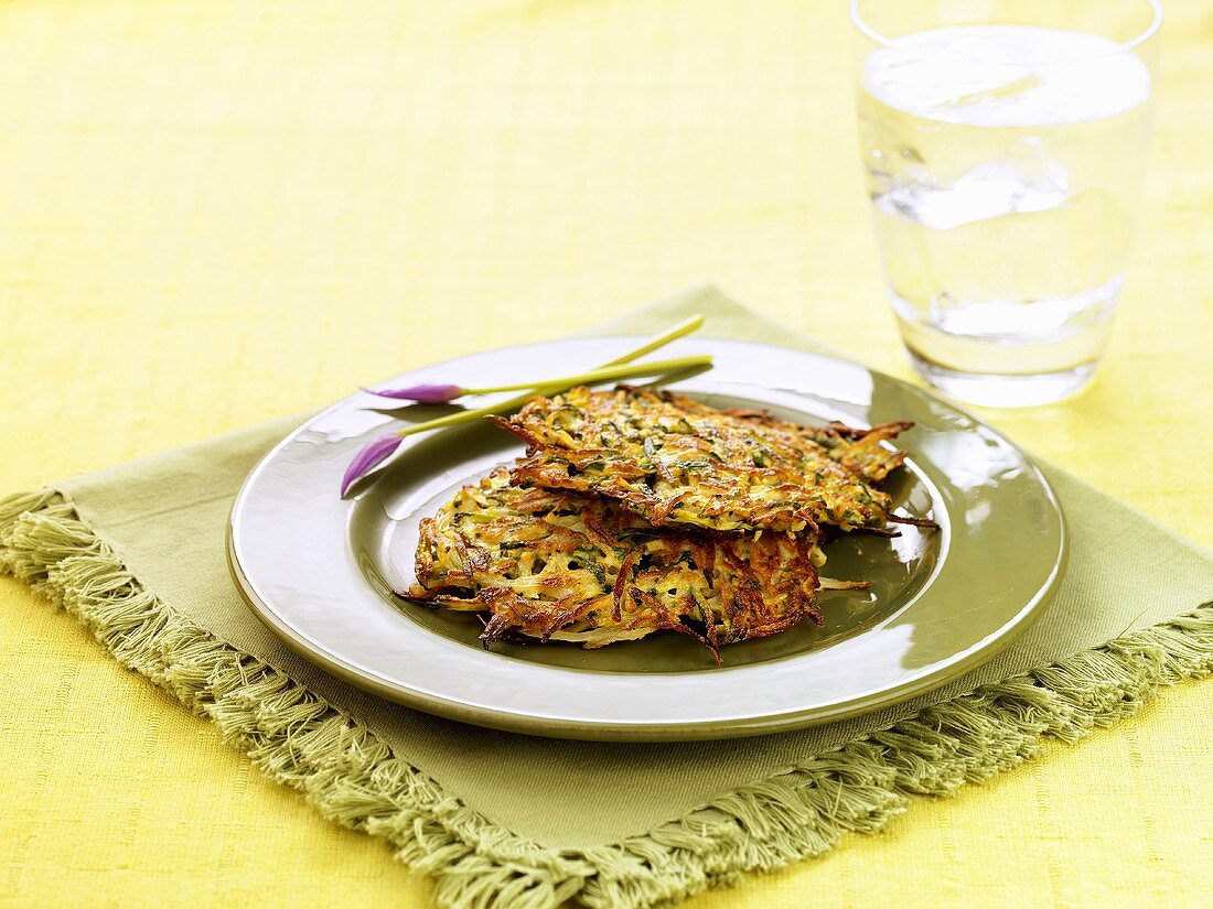 Two Zucchini Pancakes on a Plate with a Glass of Ice Water