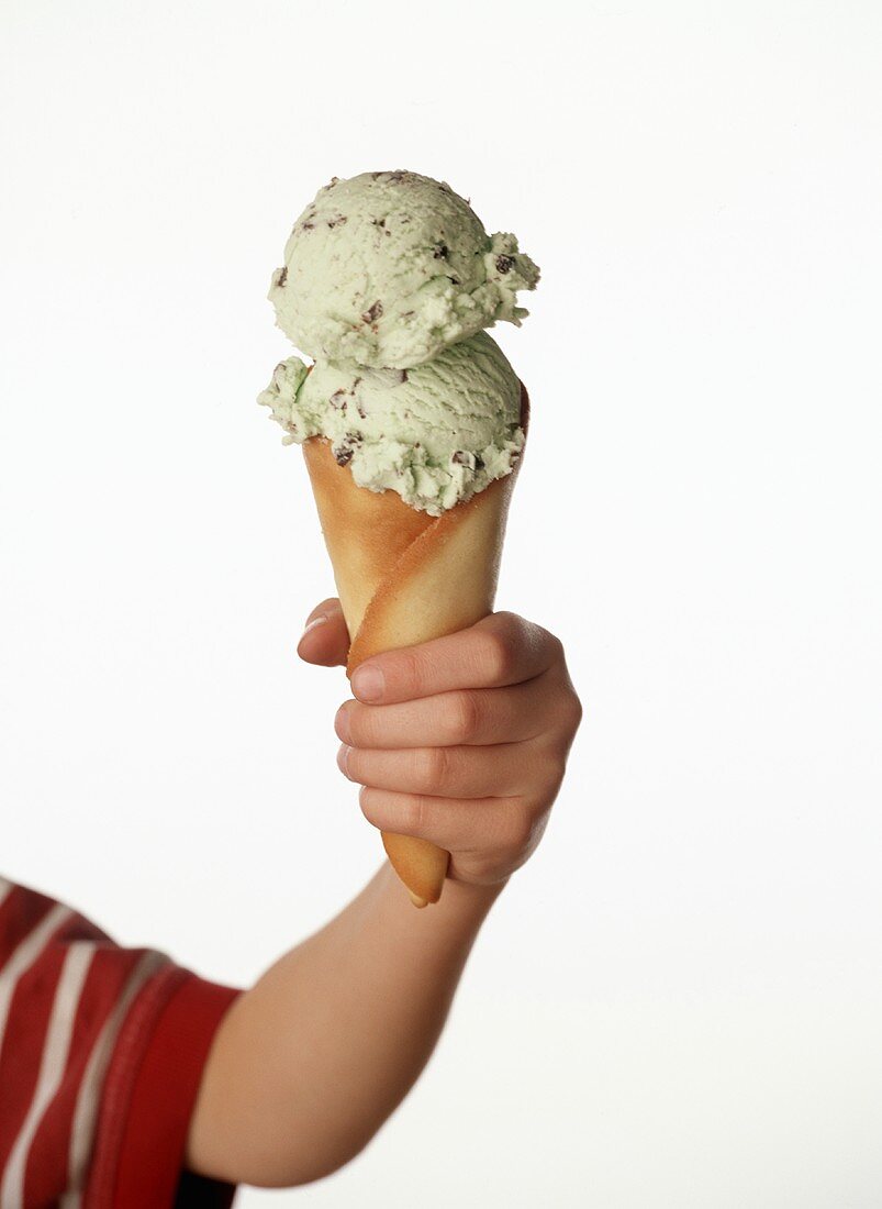 Kinderhand hält Eistüte mit Minz-Schokoladen-Eis