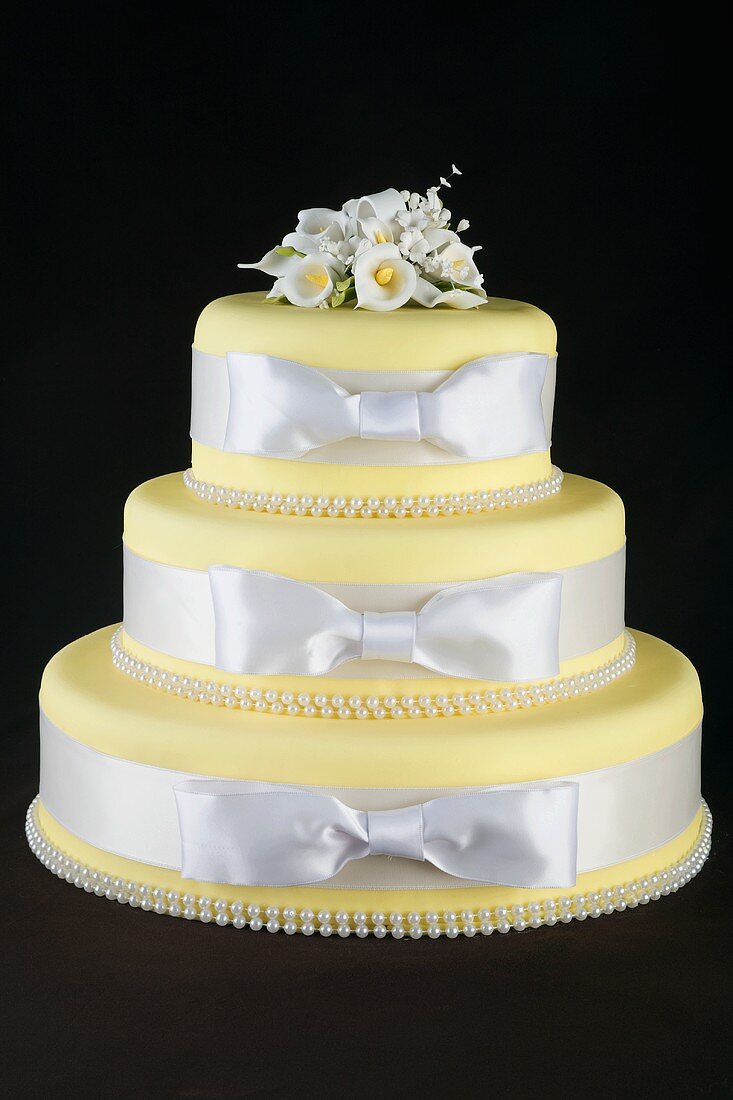 Three Tiered Yellow Cake with White Ribbon Wrapped Around Each Tier, Black Background