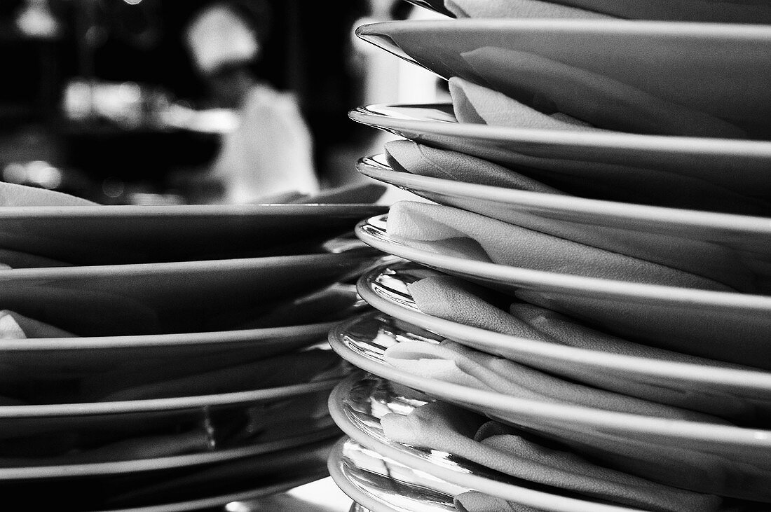 Close up of Stacked Plates in a Kitchen with Chef in Background