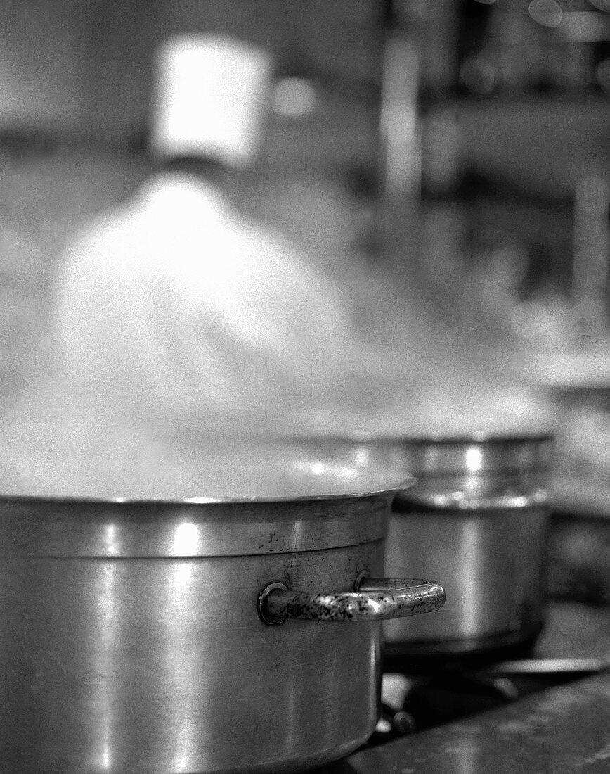 Two Steaming Stockpots on a Stovetop with Chef in Background