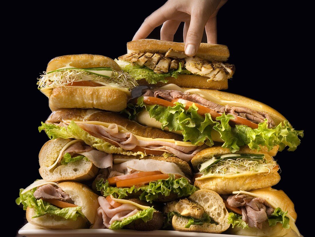 A Hand Adding to a Large Stack of Sandwiches