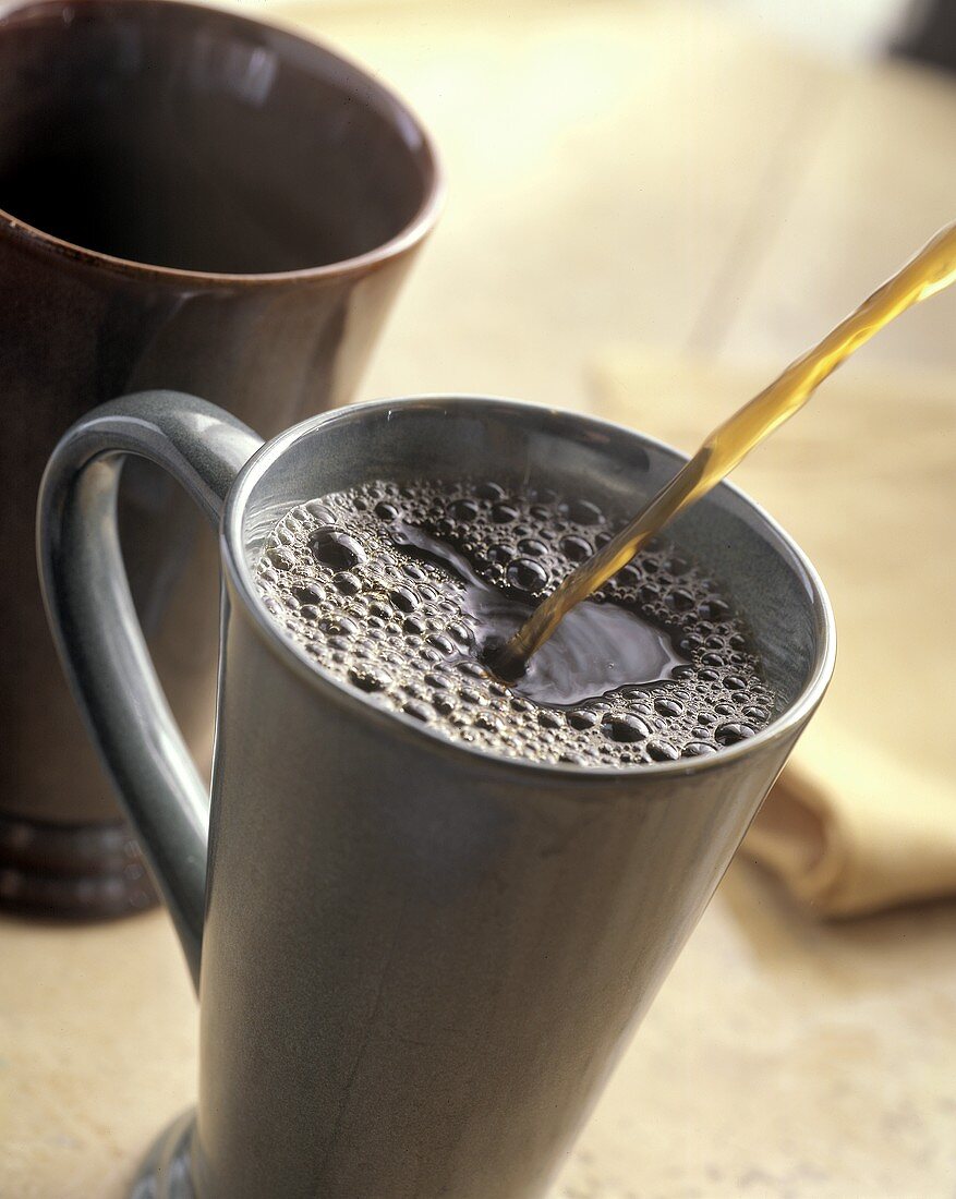 Kaffee wird in eine hohe Kaffeetasse eingeschenkt