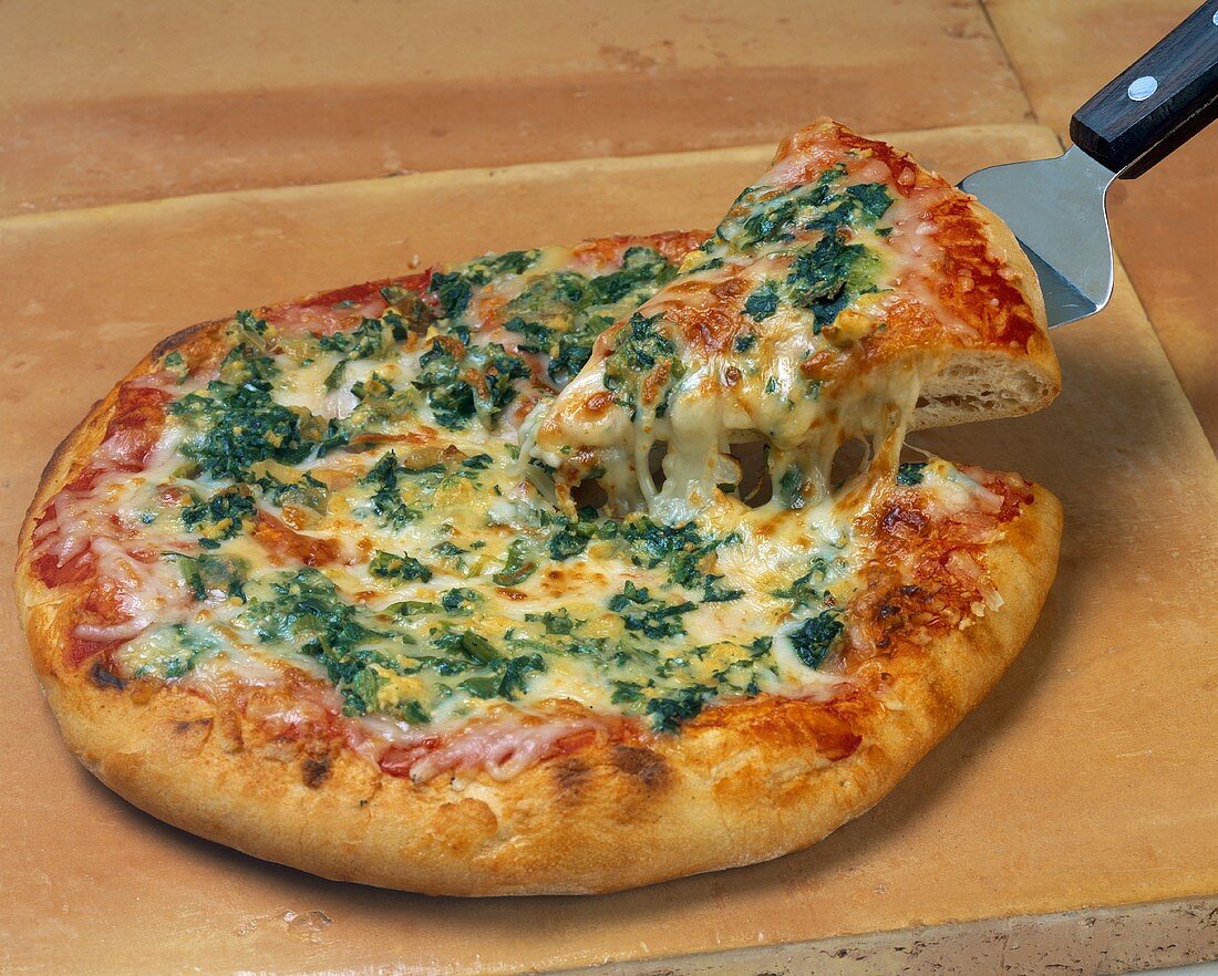 Spinach Pizza with a Piece Being Taken Out