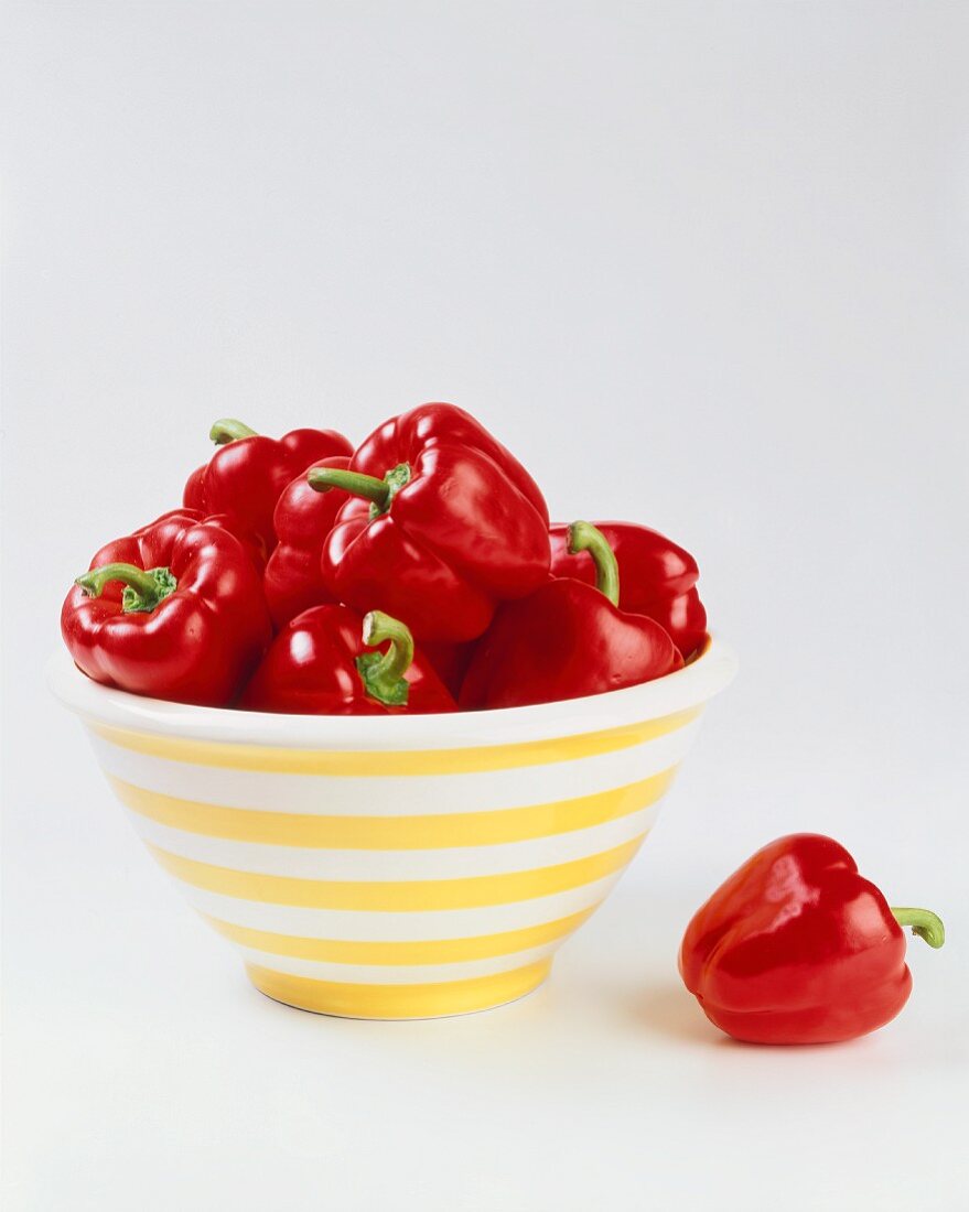 Red Bell Peppers in a Bowl; One Beside the Bowl
