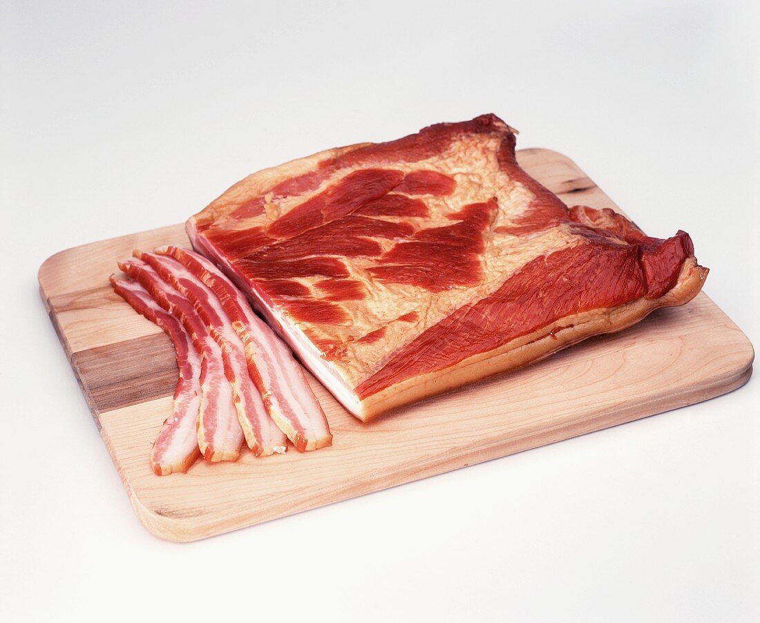 Bacon im Stück und aufgeschniiten auf Holzbrett
