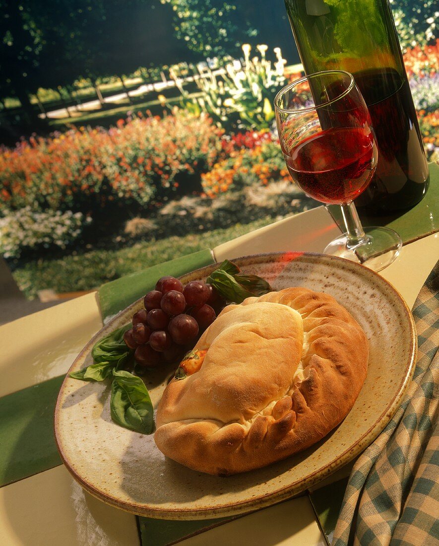 Calzone auf Teller mit Wein, im Hintergrund Parklandschaft