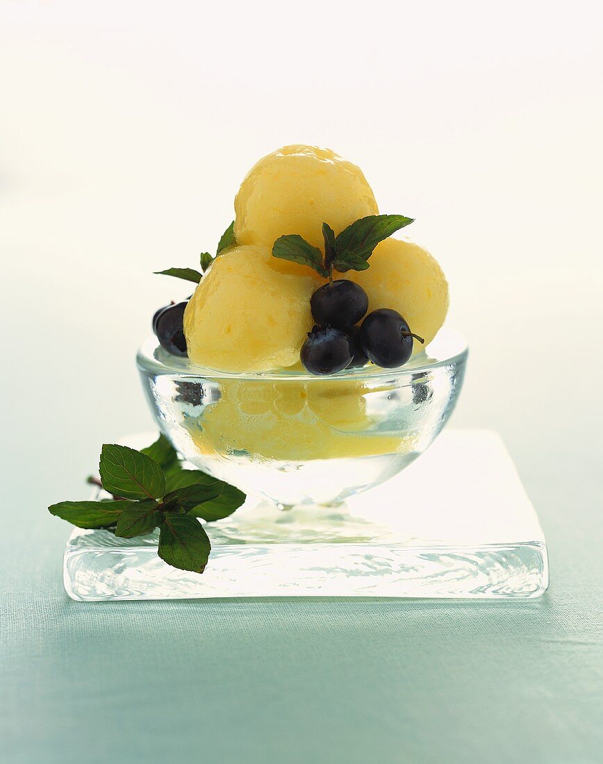 Scoops of Lemon Sorbet in a Glass Bowl Resting on Square Glass; with Blueberries and Mint