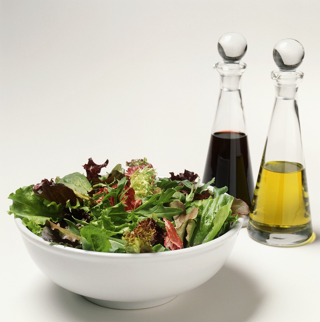 Gemischter Blattsalat dahinter Öl und Essig in Flaschen