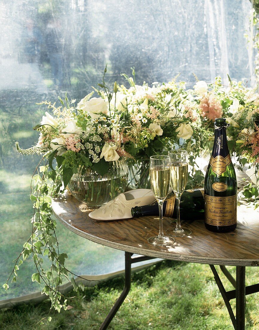 Champagnerflaschen, -gläser und Blumen auf Tisch im Garten