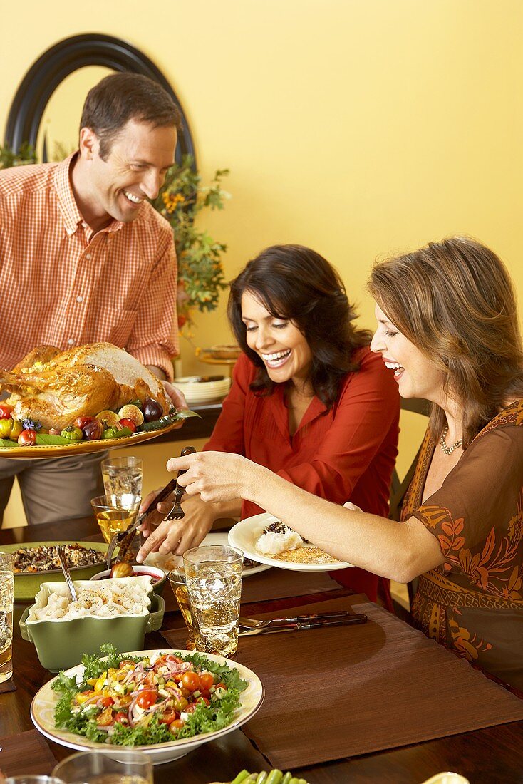 Man Holding Carved Thanksgiving Turkey While Women Serve Themselves at Thanksgiving Table