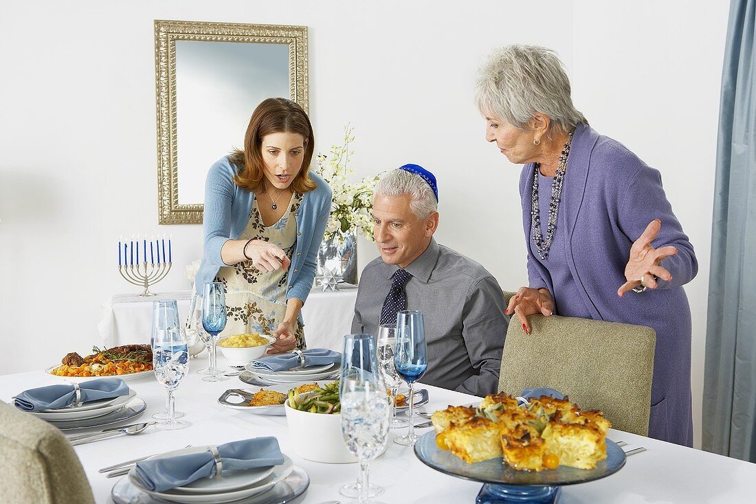 Man Sitting at Table Looking at Hanukkah Dinner Women Placed on Table
