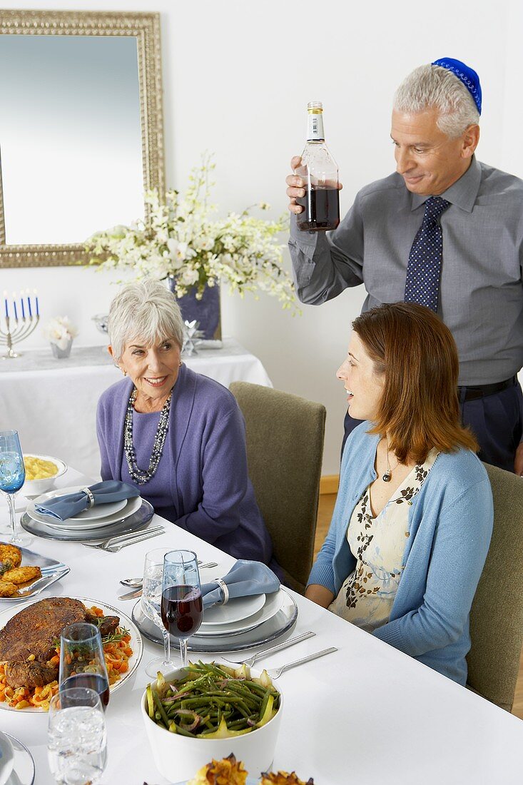 Familie am gedeckten Tisch zu Hannukah, Mann serviert Rotwein